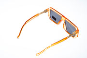 Rectangular sunglasses with a translucent amber-orange acetate frame and dark gray lenses, shown from a side angle on a white background.